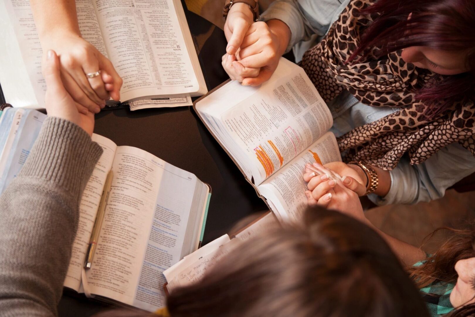 Group of students studying together, reading books and holding hands in a circle, viewed from above.