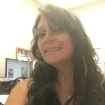 Woman smiling at the camera in an office environment with a computer monitor in the background.