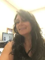 Woman smiling at the camera in an office environment with a computer monitor in the background.