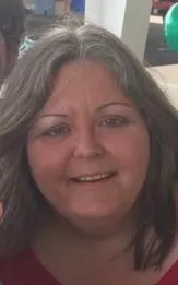 Close-up portrait of a smiling woman with shoulder-length gray hair, wearing a red top, indoors.