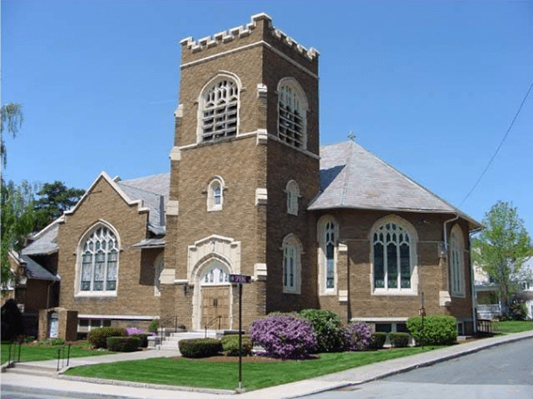 A traditional brick church with a tower, arched windows, and landscaping on a sunny day.